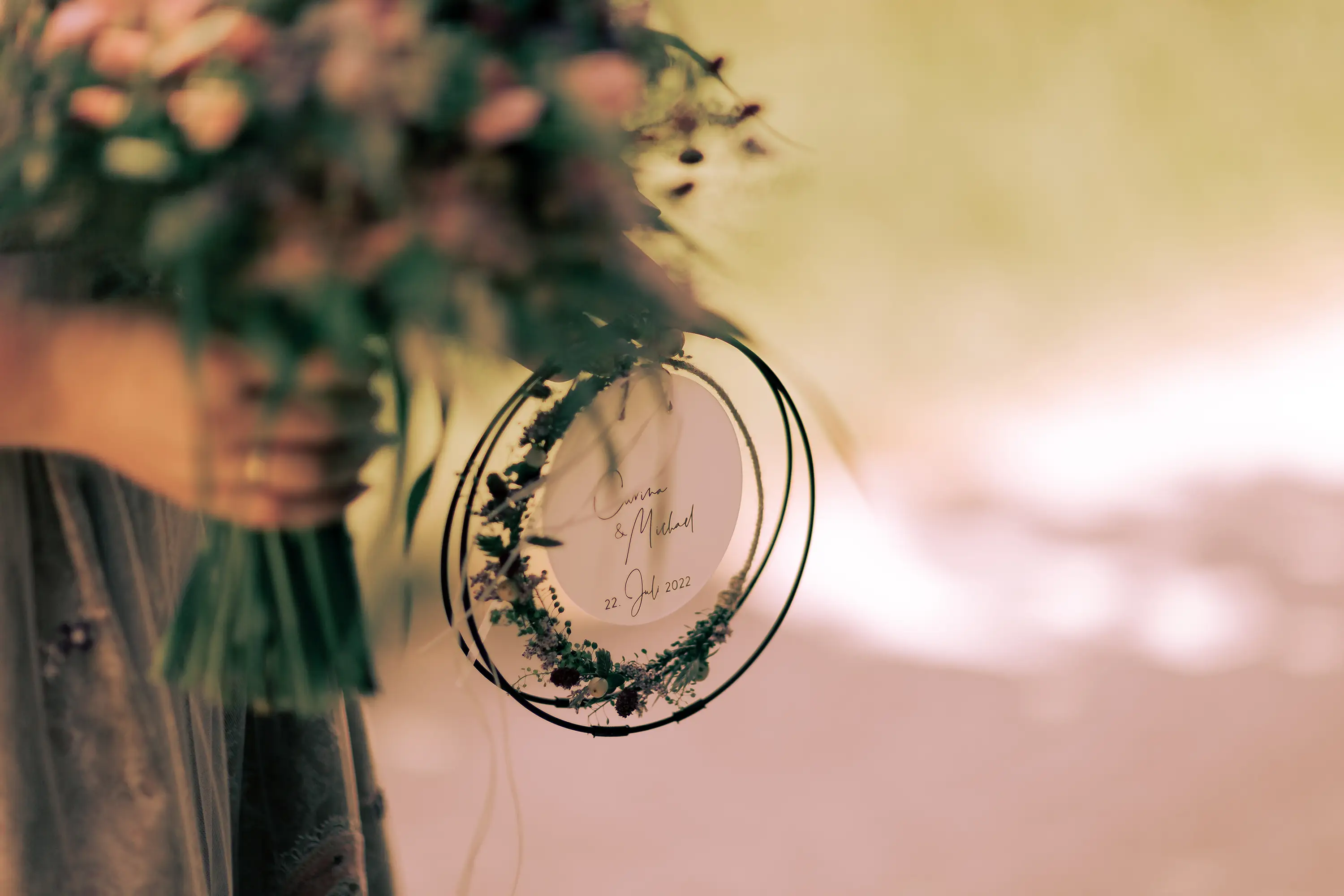 Nahaufnahme des Gestecks für die Ringe, außen ist ein Ring aus Blumen und innen ist das Hochzeitsdatum und die Namen der beiden lesbar.