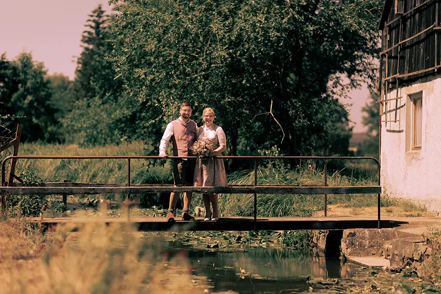Das Brautpaar steht auf einer Brücke und schaut in die Kamera.