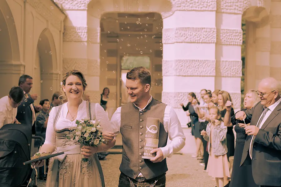Das Brautpaar läuft nach der Hochzeit durch das Spalier, man erkennt Seifenblasen im Hintergrund.