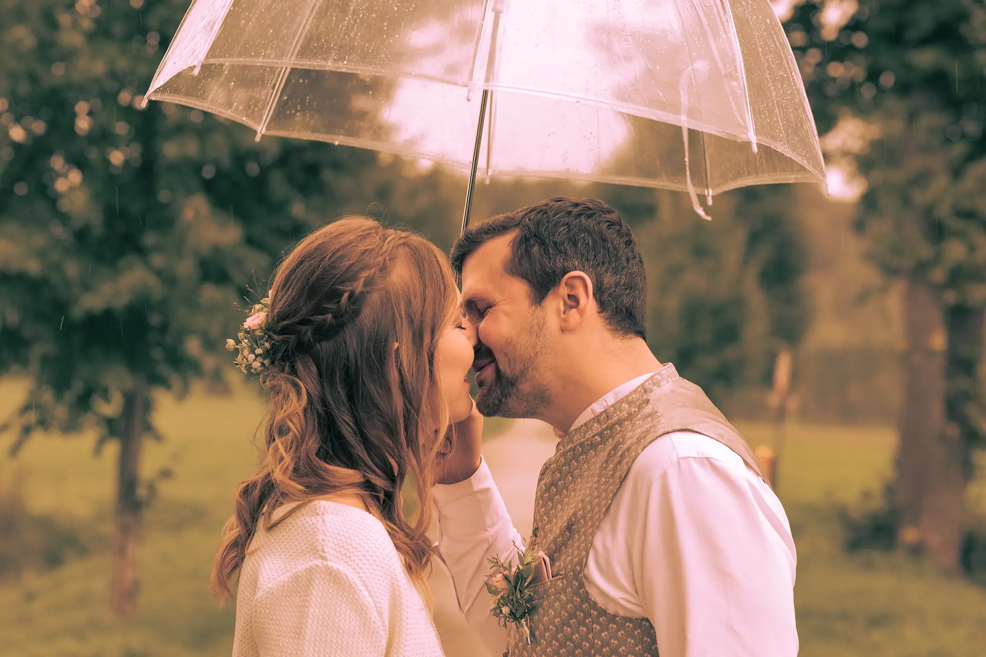 Das Brautpaar steht unter einem Regenschirm und küsst sich.