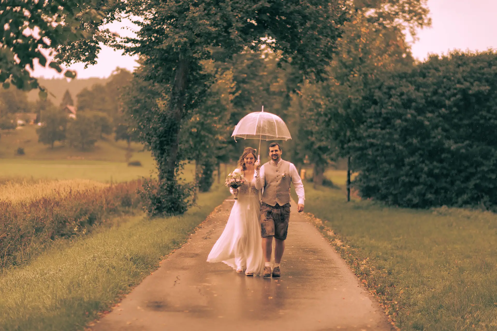 Das Brautpaar hat einen Regenschirm und läuft damit lachend durch den Regen auf die Kamera zu.