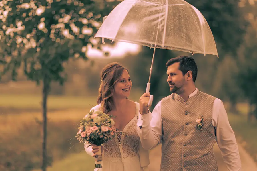Das Brautpaar hat einen Regenschirm und lächelt sich an während sie laufen.