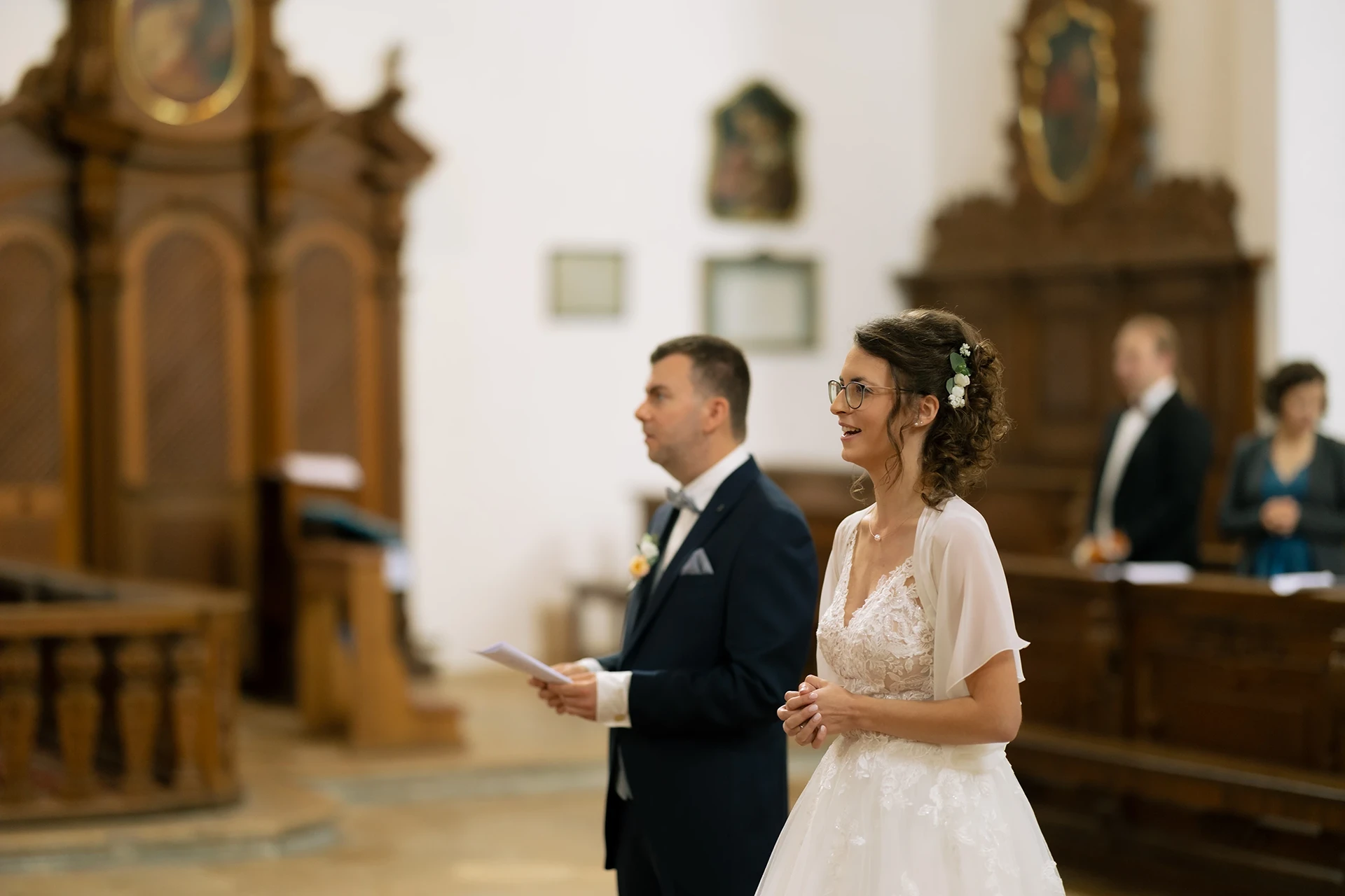 Das Brautpaar steht vorne in der Kirche, wir sehen sie leicht von der Seite.