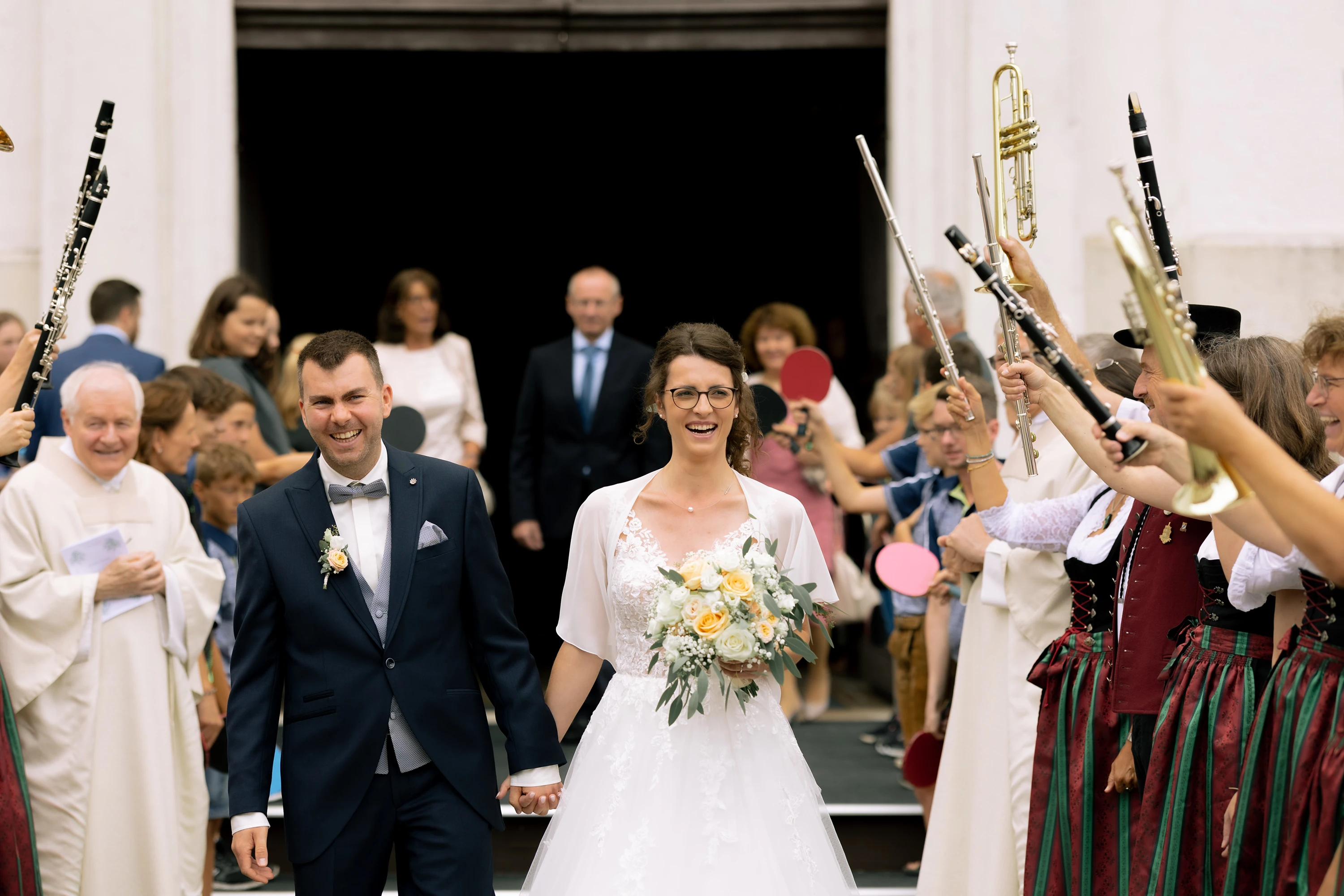Das Brautpaar tritt aus der Kirche und wird von Musikanten mit in die Höhe gehaltenen Instrumenten begrüßt.