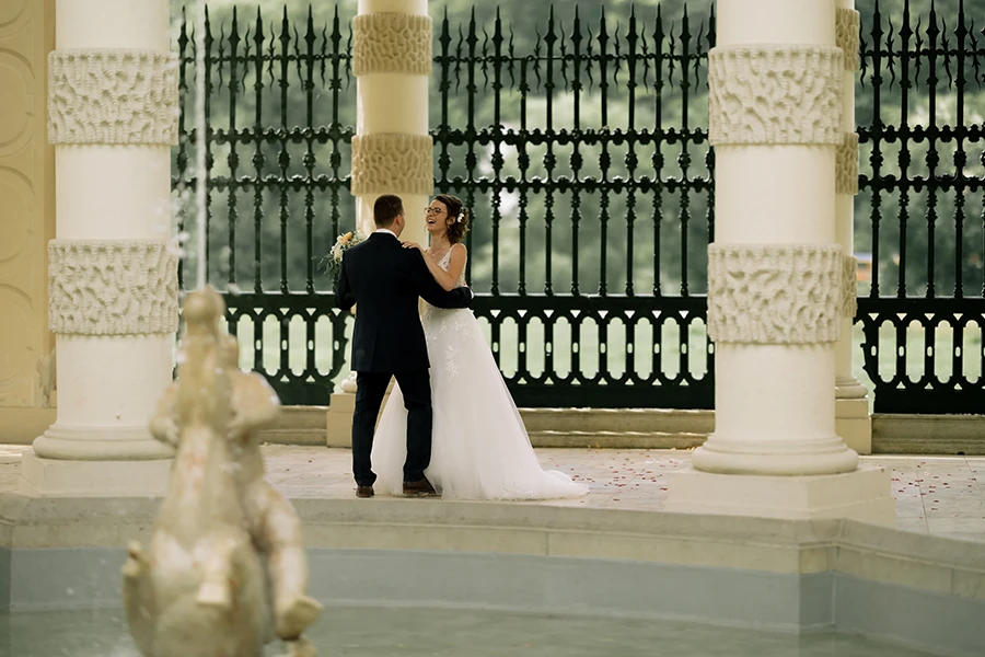 Das Brautpaar tanzt in einem Pavillon, im Vordergrund erkennt man unscharf einen Brunnen.