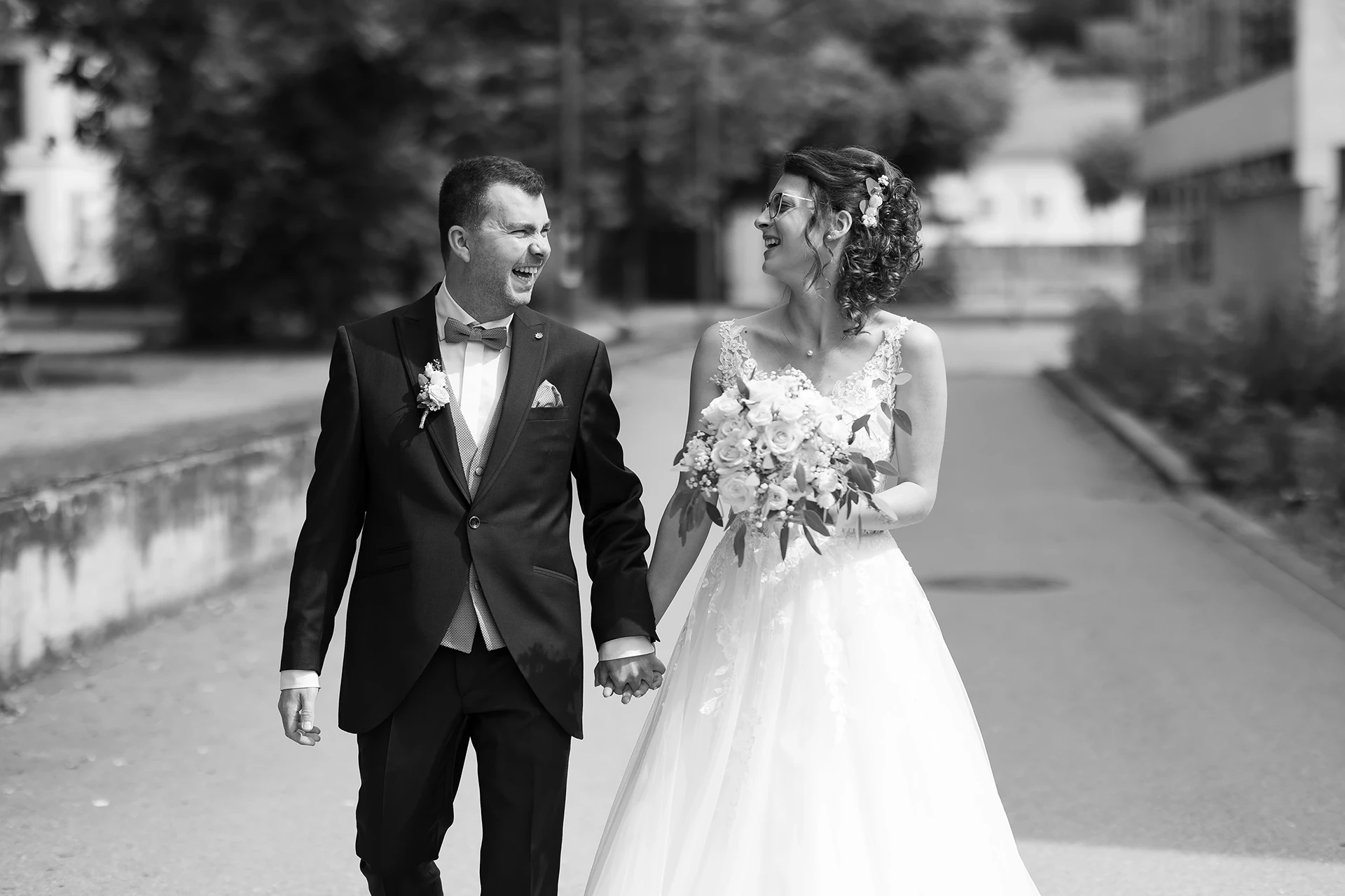 Schwarz-Weiß Aufnahme des Brautpaares von vorne, sie laufen Richtung Kamera und lachen sich gegenseitig an.