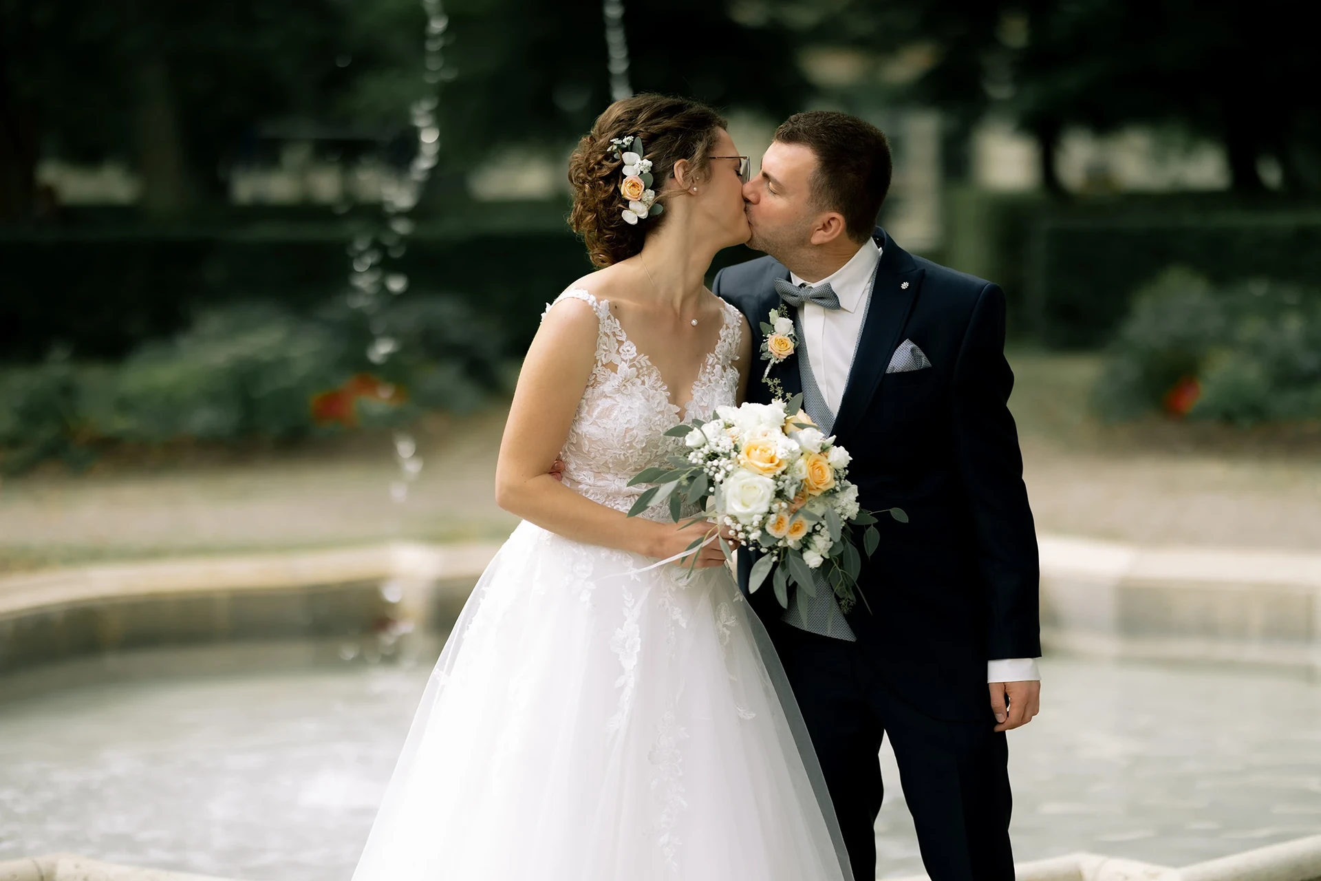 Das Brautpaar küsst sich vor einem Brunnen.