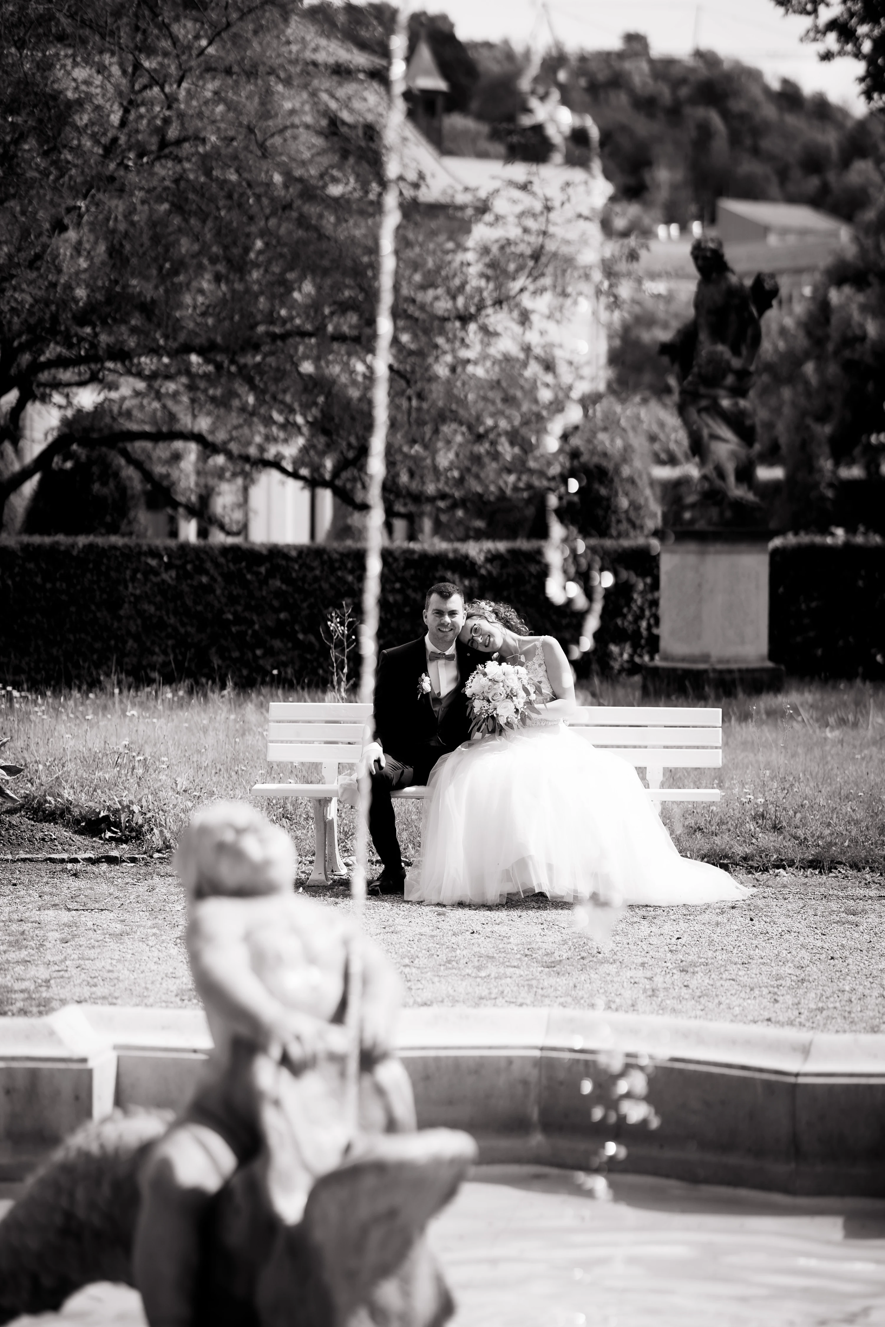 Schwarz-Weiß Hochkantaufnahme des Brautpaares, das auf einer Bank sitzt.