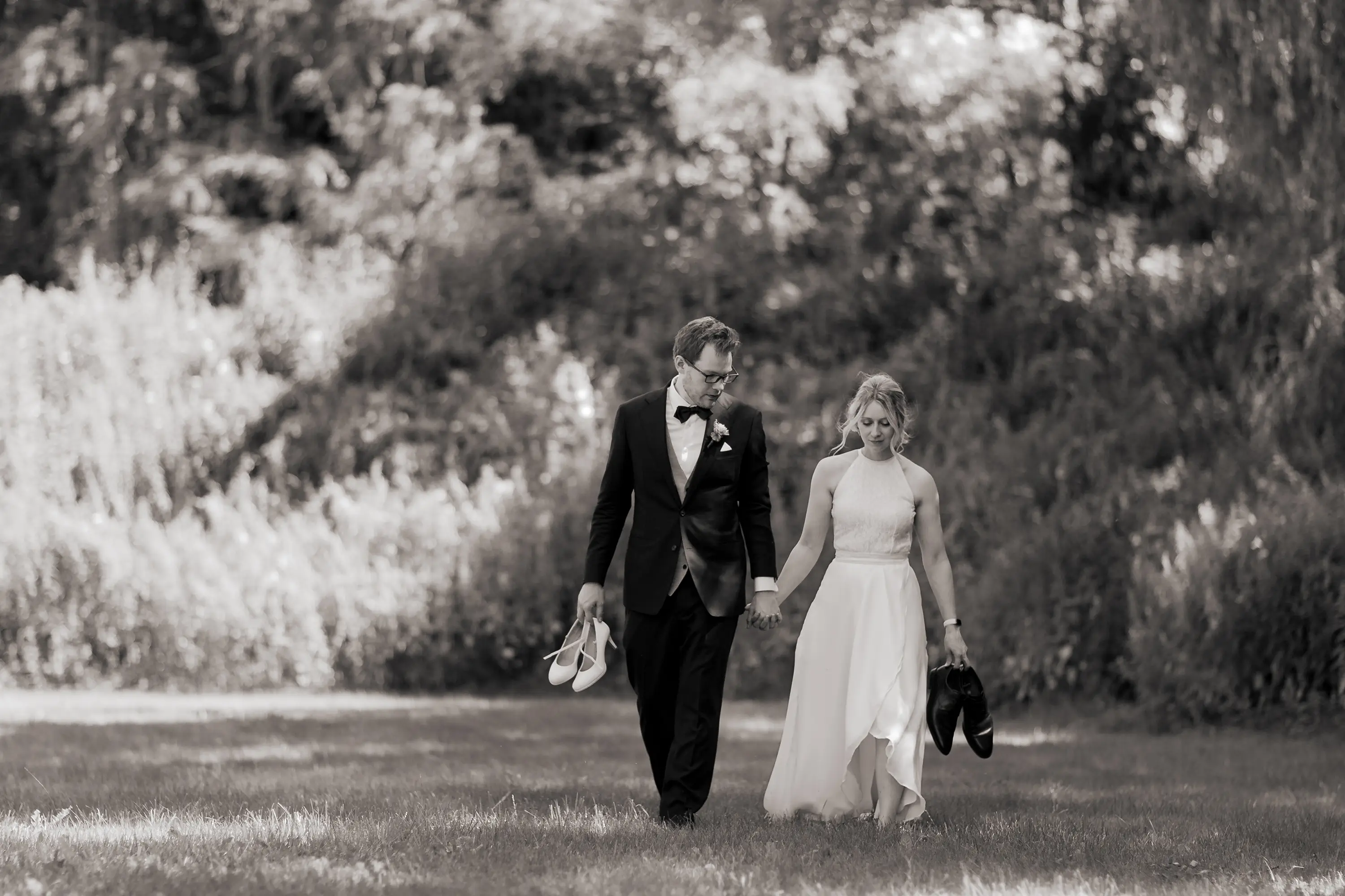 Schwarz-weiß Foto wie das Brautpaar auf die Kamera zuläuft, sie haben die Schuhe des jeweils anderen in der Hand.