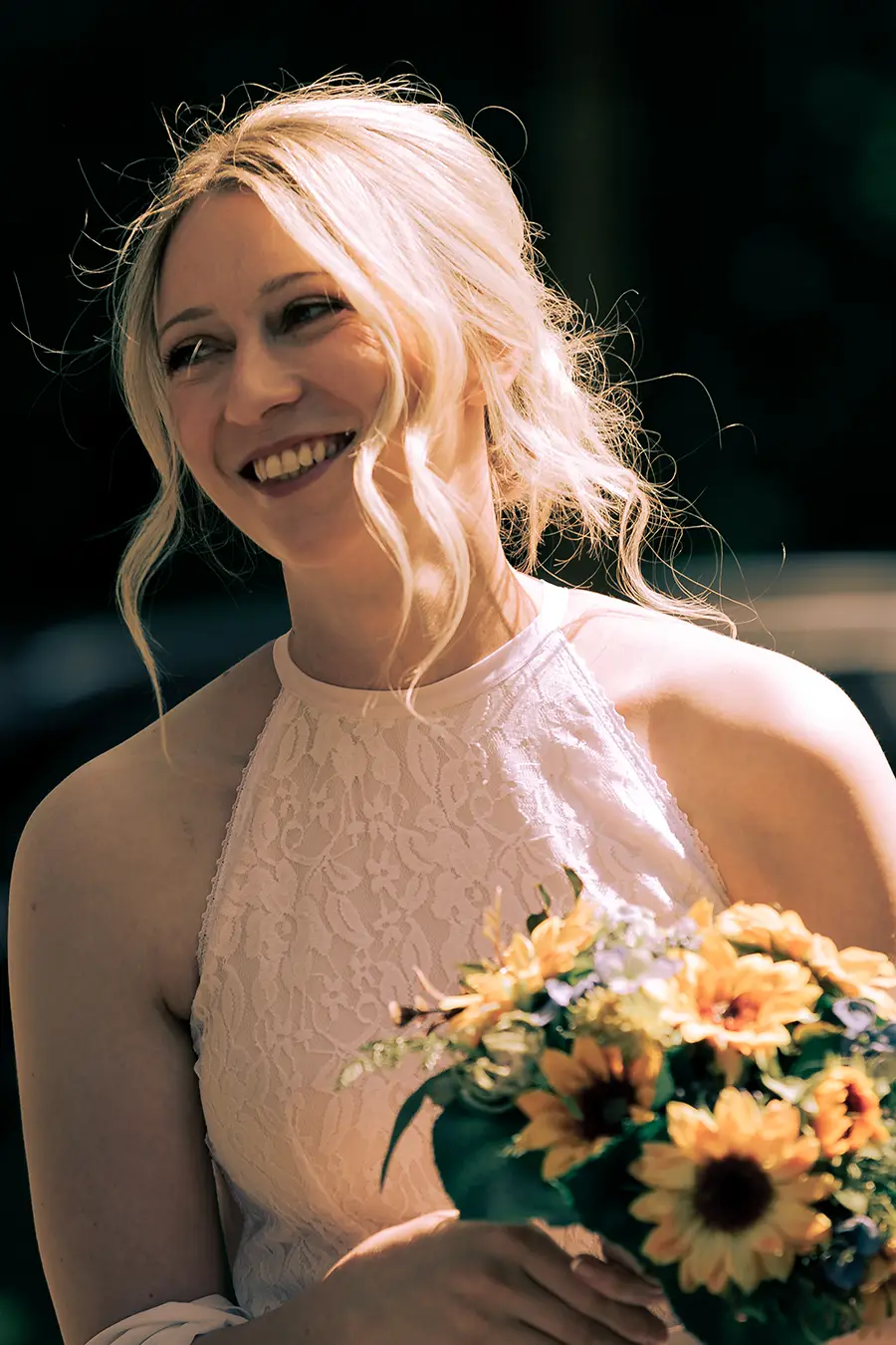 Hochkantaufnahme der Braut, die zur Seite aus dem Bild lacht, in der Hand den Brautstrauß.