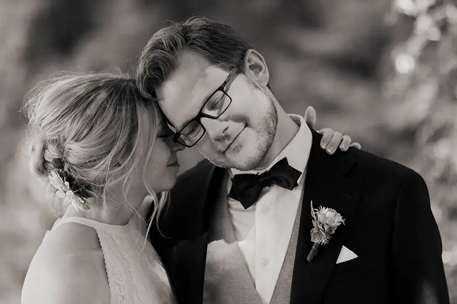 Ein schwarz-weiß Foto wie der Bräutigam sich an die Braut anlehnt.