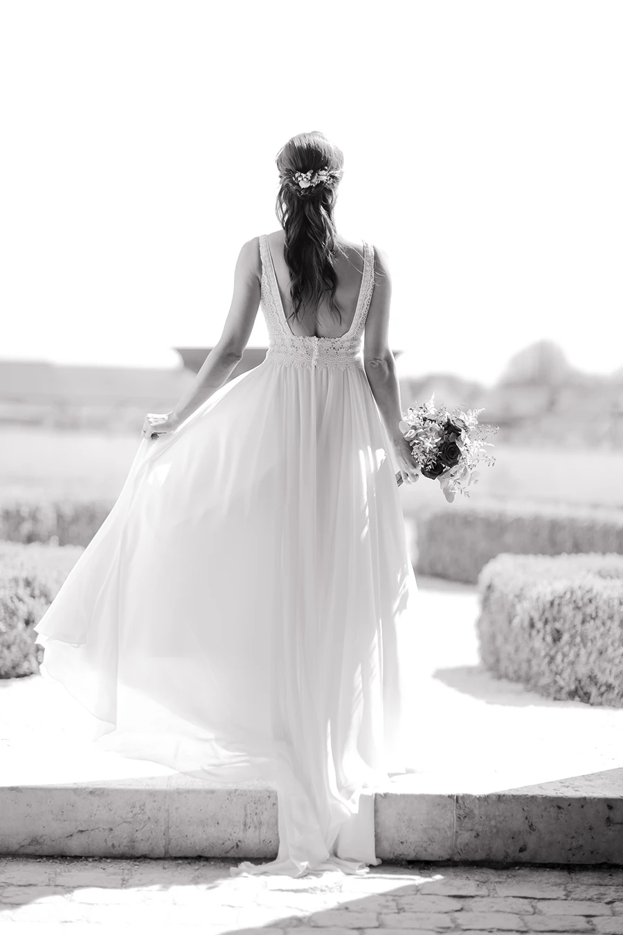 Schwarz-weiß Aufnahme der Braut von hinten, das Brautkleid fliegt im Wind.