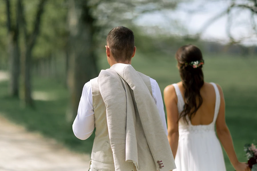 Das Brautpaar von hinten, der Bräutigam hat das Sakko über die Schulter geworfen.