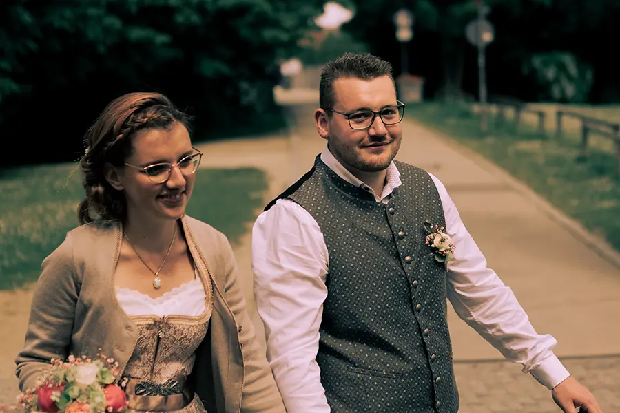 Das Brautpaar läuft durch den Klenzepark, der Bräutigam lächelt in die Kamera.