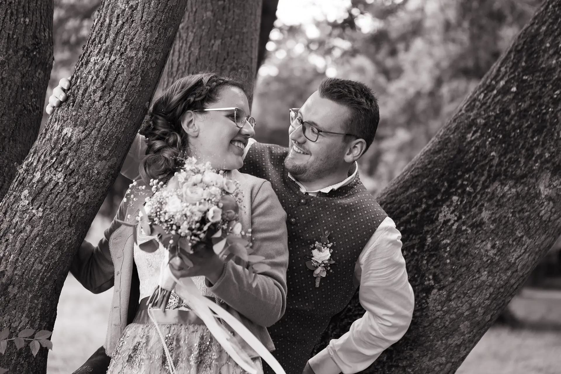 Schwarz-weiß Aufnahme des Brautpaars, das in einem Baum steht und sich über die Schultern hinweg anschaut.