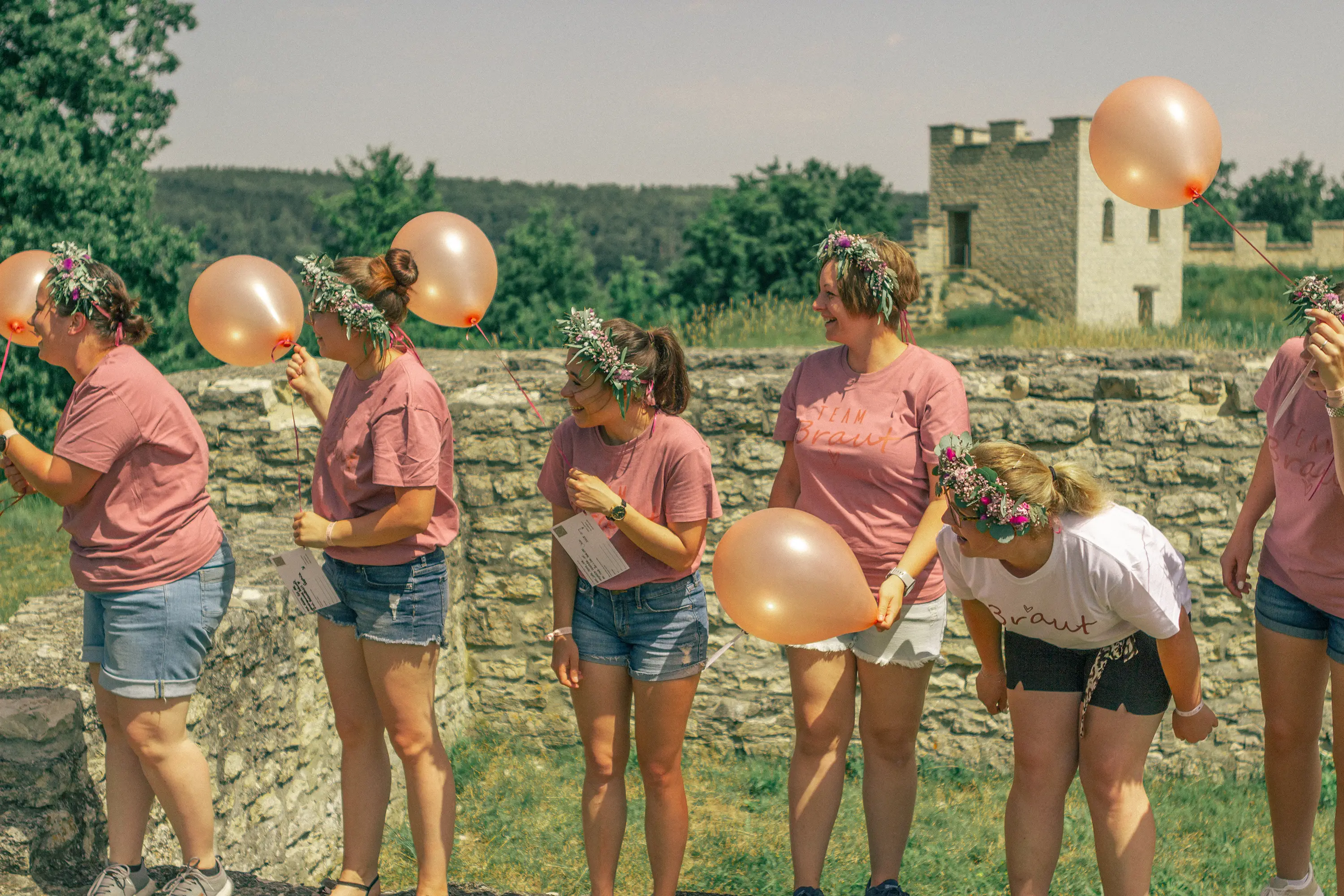 Die Mädels stehen auf einer Steinmauer mit Luftballons und schauen in eine Richtung.