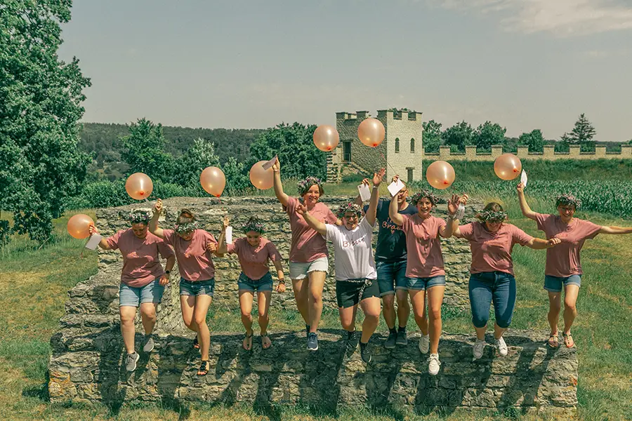 Die komplette Gruppe springt mit Luftballons in der Hand von einer Steinmauer.