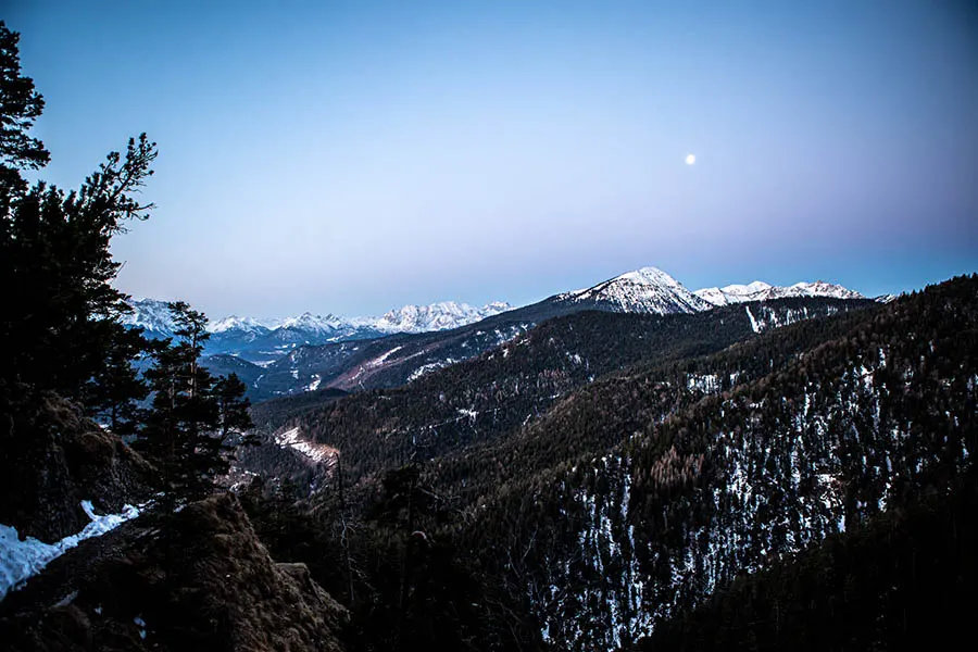 Die blaue Stunde im Winter in den Bergen, man erkennt in der Ferne den Vollmond.