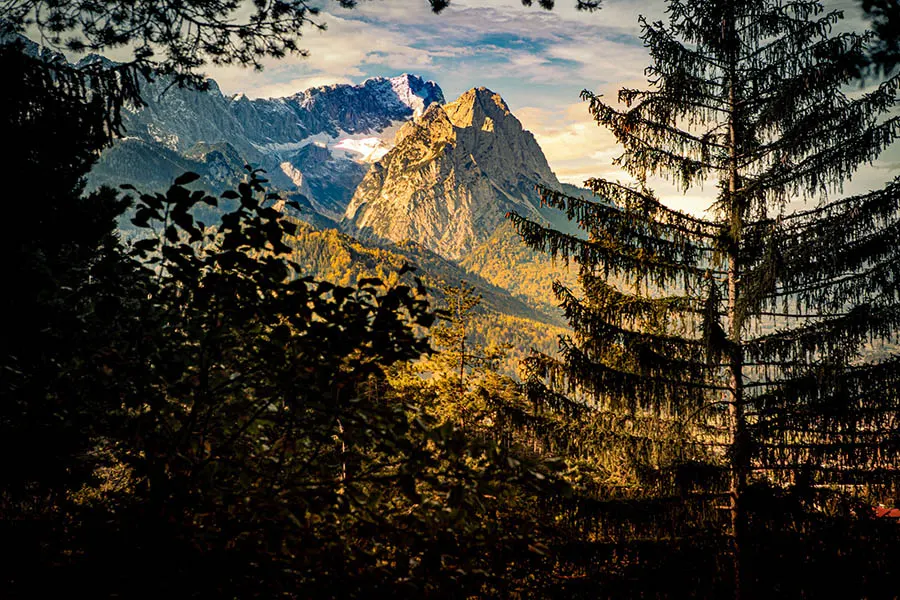 Man sieht die Gipfel der Berge Alpspitze und Zugspitze. Eine ist in gelbes, die zweite in blaues Licht getaucht.