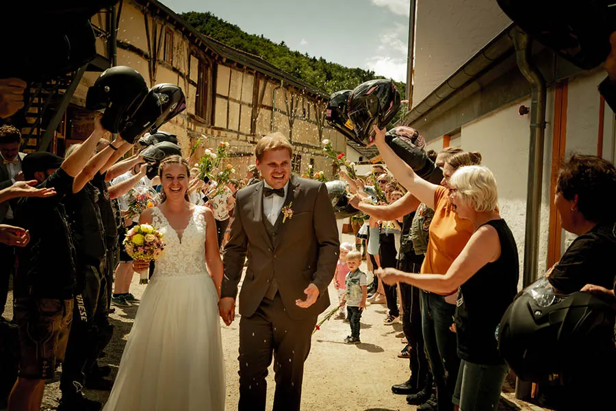 Einem Hochzeitspaar wird von Motorradfahrern Spalier gestanden, die mit ihren Helmen grüßen.